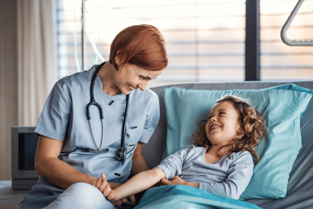 Nurse smiling down at happy young girl in hospital bed